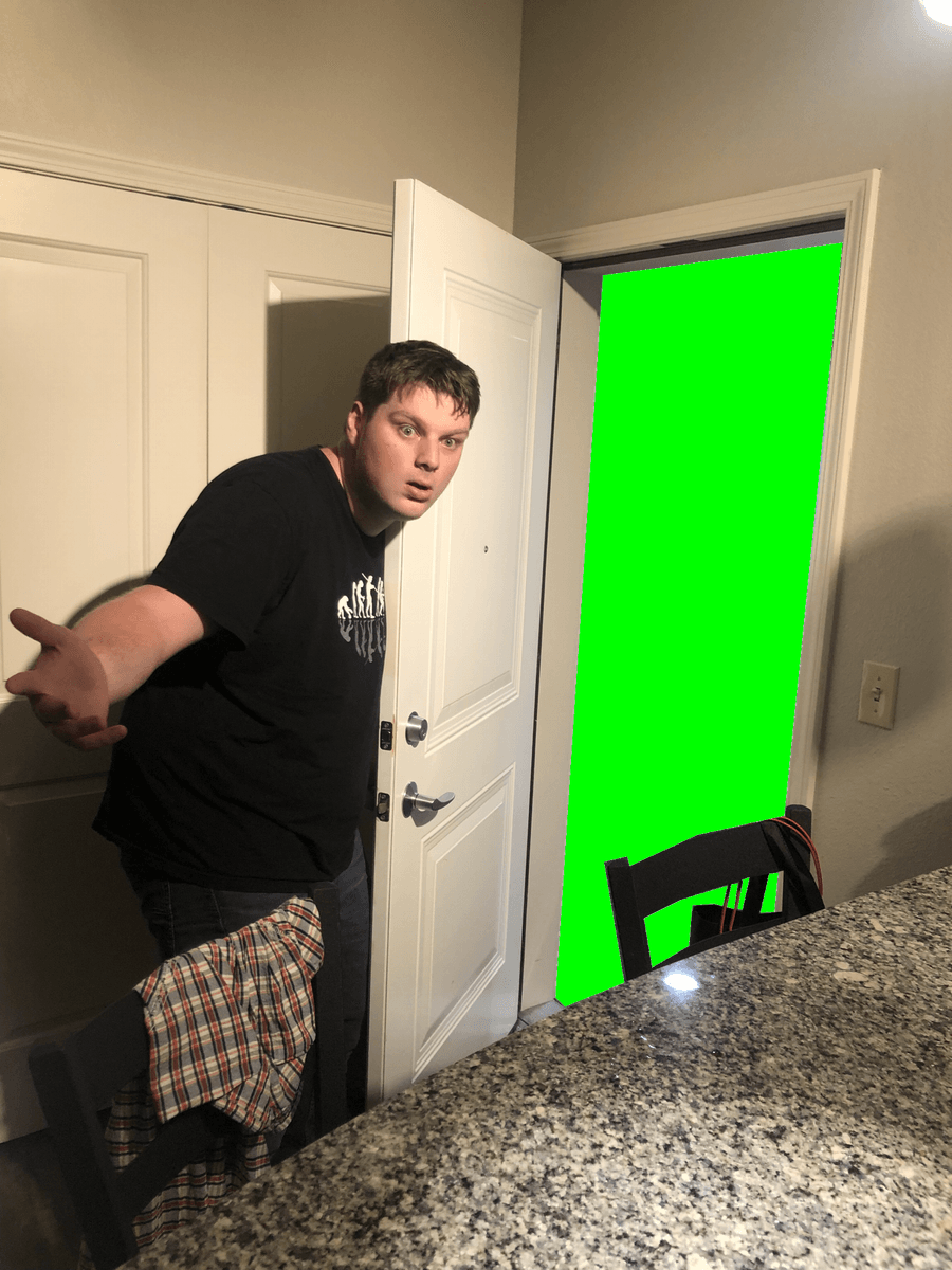 Thomas stands surprised in front of a door, leading to a green screen.